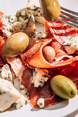 cool white wine in a glass near a plate with sliced jamon, dove cheese and various olives. a light snack on a hot day. classic italian food.