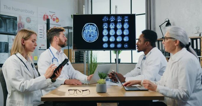 Likable confident purposeful diverse male and female medical team of neurologists holding joint consultation in medical room about patient's diagnosis using mri brain