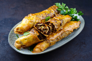 Traditional Turkish crispy sigara borek rolls with minced meat rolled in fillo pastry served as close-up in a Nordic design plate on a black board