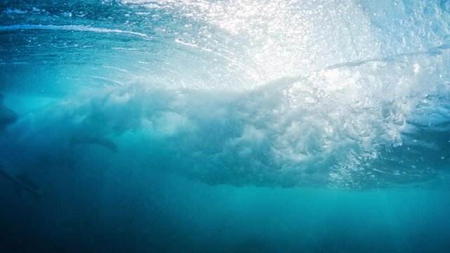 Ocean wave. Crystal clear ocean wave rolls and breaks with surfer passing it. Underwater view of the Indian Ocean's wave breaking on the Maldivian shore