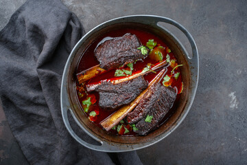 Traditionell geschmorte Rinderrippchen in Rotweinsoße serviert mit einer scharfen Chilisoße als close-up in einem Modern Design Schmortopf  - obrazy, fototapety, plakaty