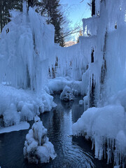 VERTICAL: Gorgeous icicles and ice formations surround a small mountain stream.