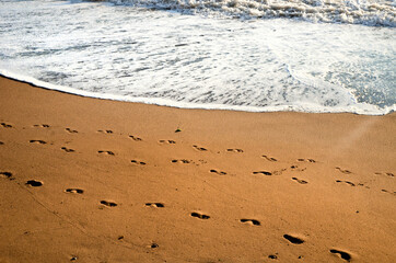 Human footprints on the sunset sandy beach. Sea waves roll ashore