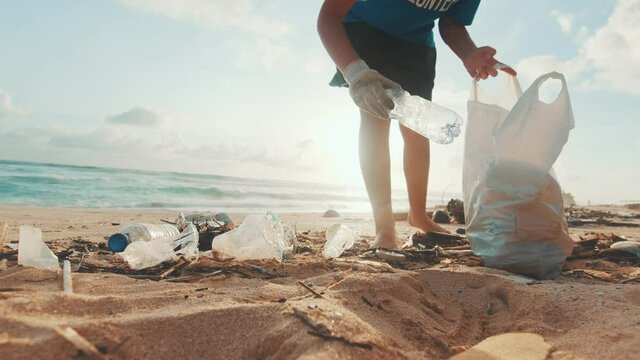 Young Caucasian woman environmental activist volunteers cleaning beach from non-degradable plastic waste saving world's oceans from pollution walks on sea sand at low tide. Caring for nature concept