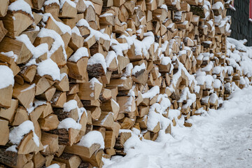 Large pile or stock of firewood for heating furnace covered with snow