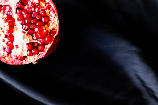 Close up photo of cut ripe red pomegranate on dark black fabric background. High quality photo