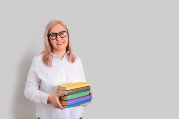 The teacher is a middle-aged woman with glasses standing on a gray background with a stack of books in her hands