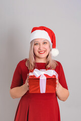 A joyful woman in a Santa hat holds a red gift box in her hands, vertical photo