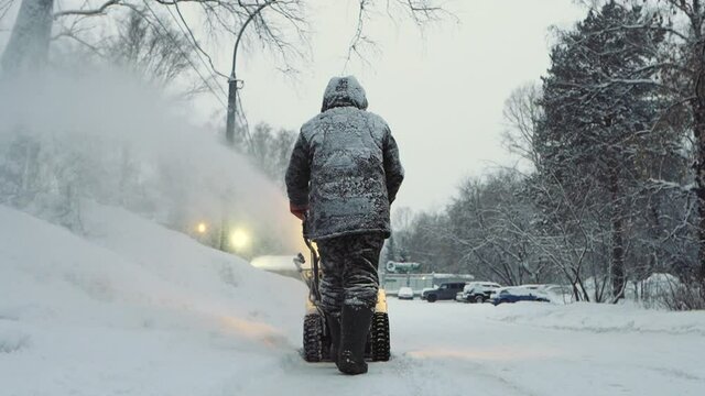 Snow-covered man cleans the road in winter with blower, snow removal equipment