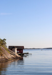 Red Swedish boathouse and pier, meeting the sea in the Stockholm archipelago, Sweden.