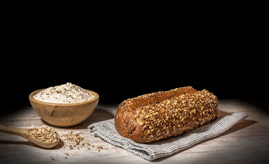 Still life of protein bread. Protein bread on black background on wooden table, with wooden bowl full of flour and wooden spoon with multiple cereals