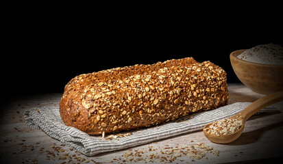 Still life of protein bread. Protein bread on black background on wooden table, with wooden bowl full of flour and wooden spoon with multiple cereals