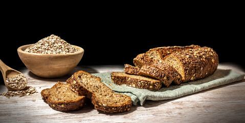 Still life of protein bread. Whole and sliced ​​protein bread, on black background on wooden table, with wooden bowl full of flour and wooden spoon with multiple cereals