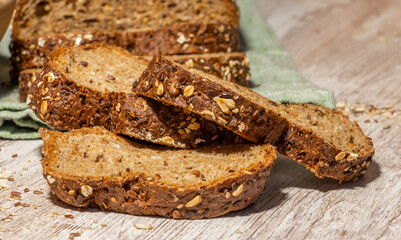 Still life of protein bread. Whole and sliced ​​protein bread, on black background on wooden table, with wooden bowl full of flour and wooden spoon with multiple cereals