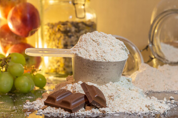 protein powder with a measuring cup and ounces of chocolate, with a light background of fruits and cereals