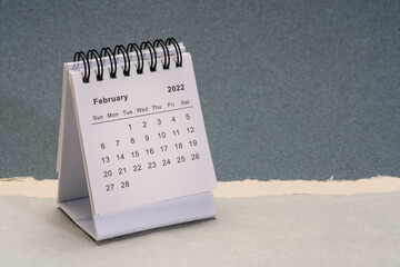 February 2022 - spiral desktop calendar  against abstract paper landscape, time and business concept