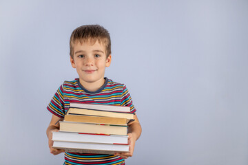 Time To Explore The Concept. A small novice schoolboy holding a stack of books on a blue studio background. Preparation for study.