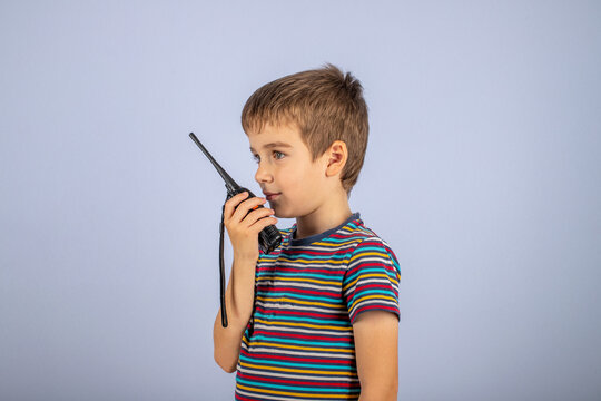 The boy is talking on the radio. A professional walkie-talkie in the child's hand. The child speaks into a walkie-talkie on a blue background.
