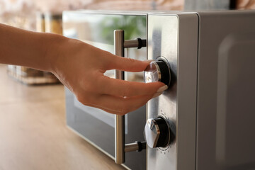 Woman switching on microwave oven in kitchen, closeup