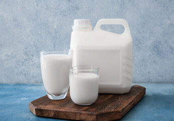 Gallon bottle and glasses of milk on color background