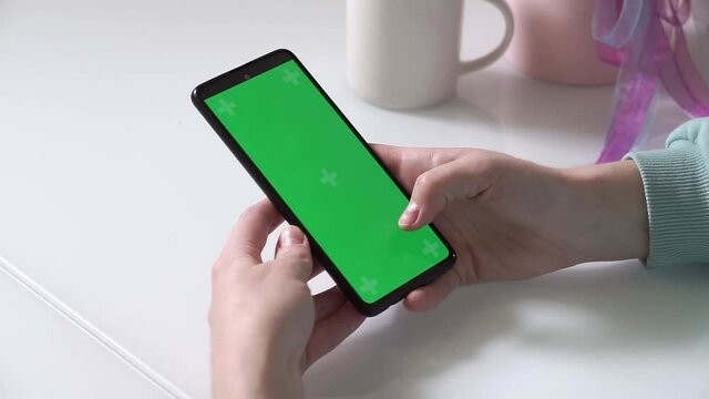Green screen chrom key. side view. Women's hands hold a smartphone with a green screen and swipe across the screen or leaf through a social network. Viewing news, e-books.
