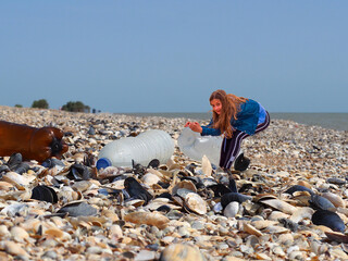 Collage on the theme of ecology. A petite girl pulls a plastic bottle thrown on a seashell beach. A reduced teenage girl on the background of huge bottles as a symbol of an environmental problem