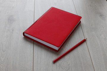 Red notebook and red pencil on a light wooden background.