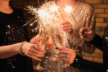 Women with glasses of champagne and Christmas lights on brick wall background, closeup