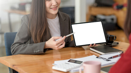 Two young businesswoman work together using a tablet blank white screen at office.