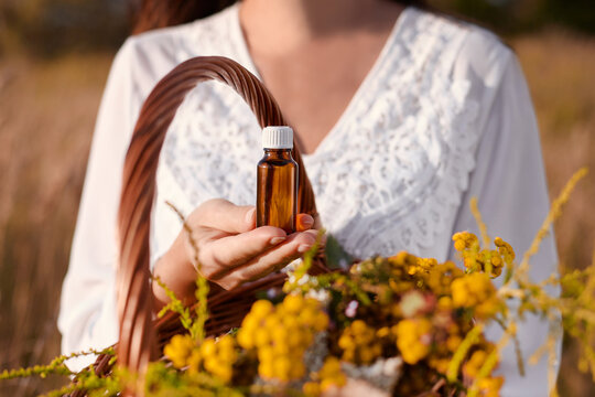 A woman holding a bottle of herbal extract. Exterior photo, natural light. Natural medicine concept.