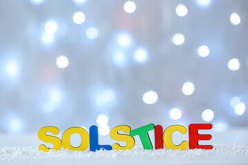 Word SOLSTICE and snow on light background with blurred lights
