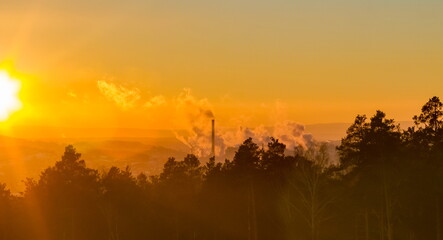 Trees and Chimneys with smoke on the background of mountains and the sunset sky in winter