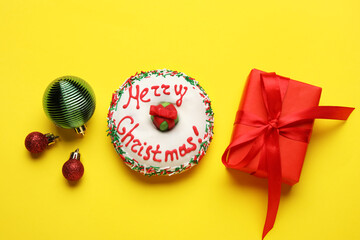 Tasty Christmas donut with balls and gift on yellow background
