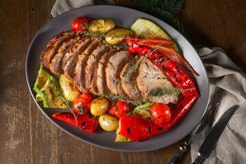 Sliced cooked pork neck on a plate with baked vegetables and potatoes on a wooden rustic table