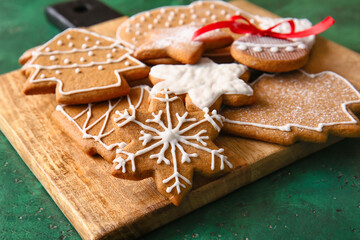 Wooden board with tasty gingerbread cookies on green background, closeup