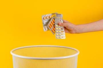 person hand holds expired medicine pills and throw it in trash bin