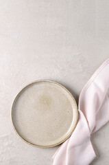 A ceramic plate and a pink napkin on a beige stone table. Top view, copy space. Table setting, menu background, mockup, recipe background, flat food mockup