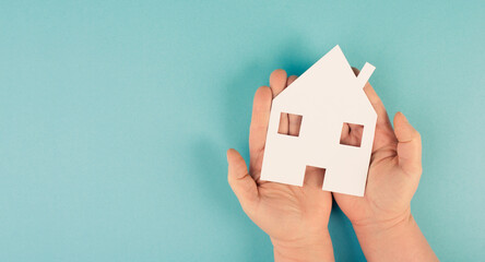 Holding a small paper house in the hands, planing to buy or rent a new home, real estate, owning...