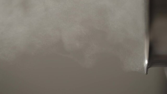Slow motion vertical shot of steam rising from steel saucepan on stove