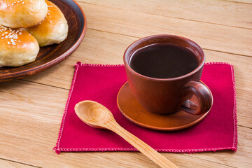 Cup of coffee and fresh fragrant buns with sesame seeds on a wooden table