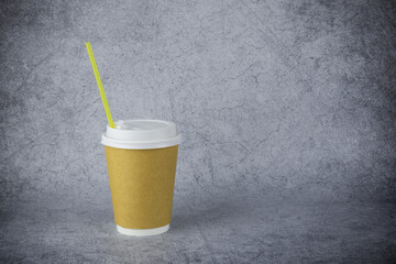 Light brown paper disposable cup with with yellow cocktail tube and white plastic lid, on gray surface