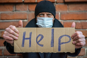 A man in an old coat and knitted hat with a sign in his hands asks for help. Social themes,...
