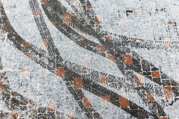 Tire prints on paving slabs covered with a thin layer of ice and fresh snow. The tracks turn and...