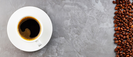 Cup of coffee on a saucer and coffee beans. Coffee and roasted coffee beans on a gray background. Coffee background. Panoramic shot