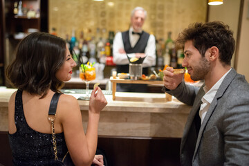 Couple eating an aperitif at a bar counter while drinking a cocktail