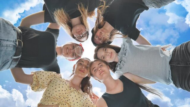 Happy girls friends hugging in a circle on the background of the fairy sky.