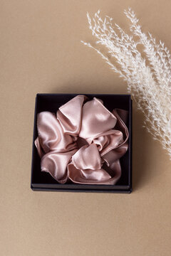 Silk hair clip in black box on beige background. Pink scrunchy. Elastic band for hair. Gift for woman