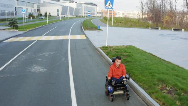 VLADIVOSTOK, RUSSIA - NOVEMBER 5, 2021: Aerial view of a man with amputated legs and arms driving on electric wheelchair along the empty street in Far Eastern Federal University campus area