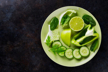 Organic green vegetables and fruits on a dark background. Green diet food on a plate. Healthy food. Top view. Copy space
