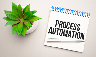 Process Automation is written in a white notepad near a clipboard, calculator, green plant, glasses and a pen on a yellow and concrete backgroundd.